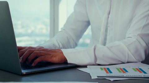 القيام بالأعمال المكتبية, مهام مكتبية في شركات الامارات العربية المتحدة، تصوير مقرب لايدي رجل عربي خليجي اماراتي يرتدي الكندورة والغترة البيضاء يستخدم الحاسوب المحمول، إنجاز مهام العمل عن بعد، إدارة شؤون الأعمال وتنظيمها عبر اللابتوب، خلفية ابراج وناطحات سحاب