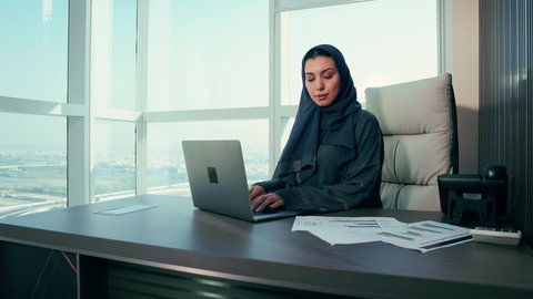 Office professions and jobs, project data auditing and analysis, monitoring the chart plan, close-up shot of an Emirati Gulf Arab woman analyzing data on a laptop, economic growth and financial investment, a Saudi woman wearing a hijab and abaya, background of skyscrapers.