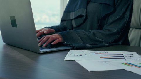 مهارة الايدي السريعة، تدقيق وتحليل بيانات المشروع، متابعة مخطط الرسم البياني، تصوير مقرب لامراه عربيه خليجيه اماراتيه تقوم بتحليل البيانات على الحاسوب المحمول، النمو الاقتصادي والاستثمار المالي، سيدة سعودية ترتدي الحجاب والعباءة، مهن ووظائف مكتبية، خلفية ناطحات سحاب