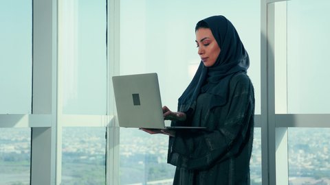 Project data auditing and analysis, monitoring the chart plan, an Emirati Gulf Arab woman analyzing data on a laptop, studying new projects, stock market fluctuations, economic growth and financial investment, a Saudi woman wearing a hijab and abaya, office professions and jobs.