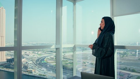 مكالمة هاتفية في مقر الشركة، تدقيق وتحليل بيانات المشروع، متابعة مخطط الرسم البياني، امراه عربيه خليجيه اماراتيه تقوم بتحليل البيانات على الحاسوب المحمول، النمو الاقتصادي والاستثمار المالي، سيدة سعودية ترتدي الحجاب والعباءة، خلفية ناطحات سحاب وابراج