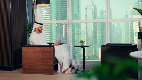 الدردشة والتواصل عبر الجوال، شركات الامارات العربية المتحدة، تصوير مقرب لايدي رجل عربي خليجي اماراتي يرتدي الكندورة والغترة البيضاء يحمل هاتف محمول، إنجاز مهام العمل عن بعد، إدارة شؤون الأعمال وتنظيمها عبر اللابتوب، خلفية ابراج وناطحات سحاب