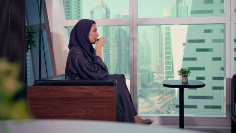 شرب المشروبات الساخنة داخل مقر الشركه، متابعة مخطط الرسم البياني، تصوير مقرب لامراه عربيه خليجيه اماراتيه تقوم بانهاء المهام اليومية، النمو الاقتصادي والاستثمار المالي، سيدة سعودية ترتدي الحجاب والعباءة، مشاركة النساء في الوظائف المكتبية، خلفية ناطحات سحاب وابراج
