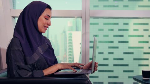 The concept of business management and holding meetings online, monitoring the chart, a close-up shot of an Emirati Gulf Arab woman working on a laptop, economic growth and financial investment, a Saudi woman wearing a hijab and abaya, background of skyscrapers and towers.
