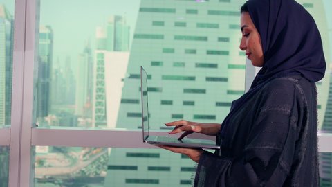 استخدام الأجهزة التقنية الحديثة،  متابعة مخطط الرسم البياني، تصوير مقرب لامراه عربيه خليجيه اماراتيه تقوم بالعمل على الحاسب المحمول، النمو الاقتصادي والاستثمار المالي، سيدة سعودية ترتدي الحجاب والعباءة، خلفية ناطحات سحاب وابراج، الاناقة ولاهتمام بالمظهر الخارجي