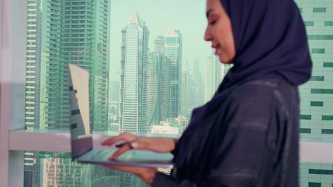 A profession and job for women, monitoring a chart, a close-up shot of an Arab Gulf Emirati woman working on a laptop, economic growth and financial investment, a Saudi woman wearing a hijab and abaya, a background of skyscrapers and towers, elegance and attention to appearance.