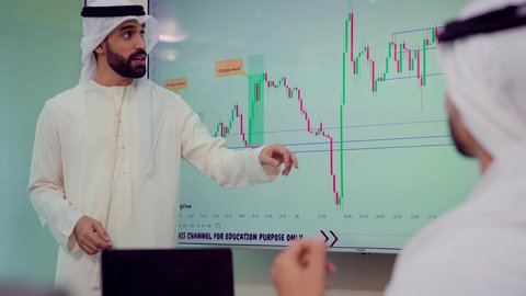 Study of statistical data sheets, gestures of self-confidence, integrating modern technical devices into office work, developing projects and investments, managing and dividing tasks, explaining and analyzing charts, a Gulf Arab Emirati team conducting a business meeting inside the conference room at the company's headquarters.
