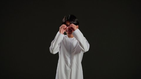 التخطيط المستقبلي للأهداف والطموحات، رؤية الاشياء البعيدة، حب المغامرة والاستكشاف، بورتريه لولد عربي خليجي سعودي يرتدي الثوب الابيض يضع يديه على عينه على شكل منظار ثنائي العينين، تعابير الفرح والسرور, خلفية سوداء