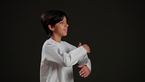 الاهتمام بالمظهر الخارجي، بورتريه لولد عربي خليجي سعودي يرتدي الثوب الابيض يقف بأيدي متقاطعه ينظر إلى الكاميرا بتعابير الثقة بالنفس ,خلفية سوداء