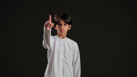 مفهوم الرفض والامتناع ، تحديد موقع معين, الإشارة و التوضيح إلى شيء ما، بورتريه لولد عربي خليجي سعودي يرتدي الثوب الابيض يشير بإصبع السبابة إلى شيء ما ينظر اليه, خلفية سوداء