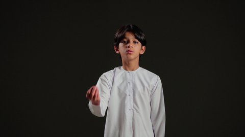 الهدوء وطلب التوقف، بورتريه لولد عربي خليجي سعودي يرتدي الثوب الابيض يشير بيدية بإيماءات الصبر والتأن والتريث، إمهال الوقت والإنتظار للقيام بشيء ما، خلفية سوداء