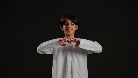 إظهار مشاعر الحب و الشغف، مفهوم المحبة و المودة, النظر إلى الكاميرا بإيماءات السعادة و السرور, بورتريه لولد عربي خليجي سعودي يرتدي الثوب الابيض يشكل بيديه شكل قلب, خلفية سوداء