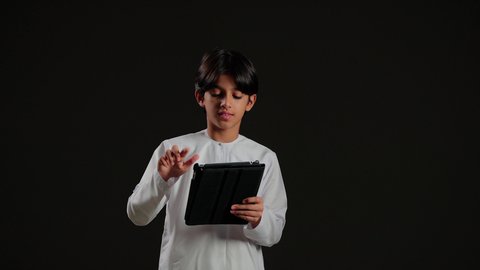 تصفح مواقع التواصل الاجتماعي، بورتريه لولد عربي خليجي سعودي يرتدي الثوب الابيض يحمل بيده جهاز التابلت، استخدام التقنية الحديثة في تزويد الأجيال بالمعلومات المفيدة، خلفية سوداء