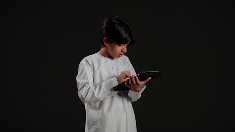 استخدام التقنية الحديثة في تزويد الأجيال بالمعلومات المفيدة،  تصفح مواقع التواصل الاجتماعي، بورتريه لولد عربي خليجي سعودي يرتدي الثوب الابيض يحمل بيده جهاز التابلت، خلفية سوداء