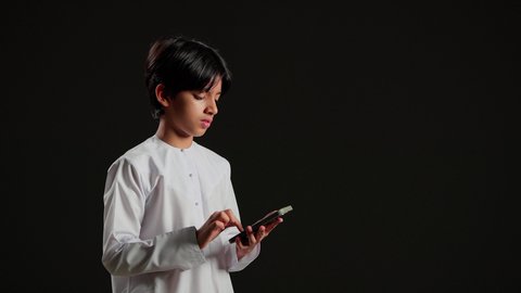 إجراء مكالمة هاتفية باستخدام الموبايل، تبادل الأخبار مع الأهل والأصدقاء، بورتريه لولد عربي خليجي سعودي يرتدي الثوب الابيض يقوم بالتواصل مع الأقارب، تعابير السعادة و السرور، خلفية سوداء