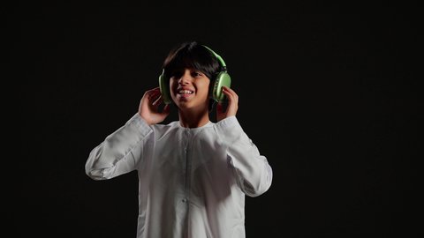 التفاعل والاندماج مع الأنغام الموسيقية، استخدام الأجهزة التقنية الحديثة، الاستماع الى الأغاني والموسيقى عبر سماعة الرأس، بورتريه لولد عربي خليجي سعودي يرتدي الثوب الابيض يضع الهيدفون يقوم بالإصغاء إلى شيء ما، خلفية سوداء