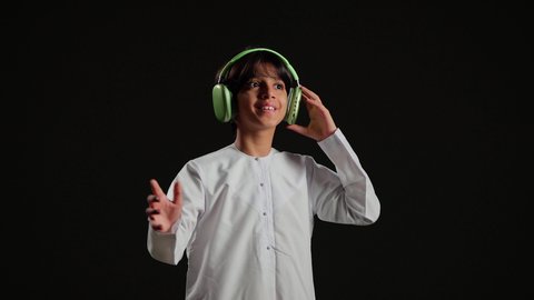 استخدام الأجهزة التقنية الحديثة، التفاعل والاندماج مع الأنغام الموسيقية، الاستماع الى الأغاني والموسيقى عبر سماعة الرأس، بورتريه لولد عربي خليجي سعودي يرتدي الثوب الابيض يضع الهيدفون يقوم بالإصغاء إلى شيء ما، خلفية سوداء