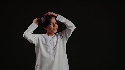 المحافظة على شعر صحي وأنيق، العناية والاهتمام بالجمال والأناقة والمظهر الخارجي، بورتريه لولد عربي خليجي سعودي يرتدي الثوب الابيض يقوم بتصفيف وتمشيط الشعرباستخدام الفرشاة ( المشط )، خلفية سوداء