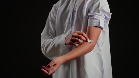 وجود الآلام والأوجاع,، وضع الضمادات الطبية مكان الإصابة لتخفيف الألم, بورتريه مقرب لفتى عربي خليجي سعودي يرتدي الثوب الابيض يضع ضمادة الجروح  , التضميد الصحيح للجراح, خلفية سوداء