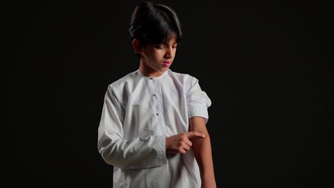 وضع الضمادات الطبية مكان الإصابة لتخفيف الألم, بورتريه مقرب لفتى عربي خليجي سعودي يرتدي الثوب الابيض يضع ضمادة الجروح بإيماءات التألم , وجود الآلام والأوجاع, التضميد الصحيح للجراح, خلفية سوداء