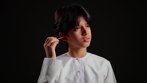 روتين نظافة الأذنين اليومية، العناية والاهتمام بصحة الأذن، استخدام أعواد ونكاشات القطن، بورتريه مقرب لفتى عربي خليجي سعودي يرتدي الثوب الابيض يقوم وضع نكاشة قطنية داخل أذنه، الاهتمام المظهر الخارجي، خلفية سوداء