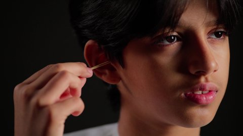 العناية والاهتمام بصحة الأذن، روتين نظافة الأذنين اليومية، استخدام أعواد ونكاشات القطن، بورتريه مقرب لفتى عربي خليجي سعودي يرتدي الثوب الابيض يقوم وضع نكاشة قطنية داخل أذنه، الاهتمام المظهر الخارجي، خلفية سوداء