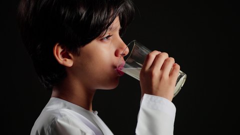 المحافظة على سلامة الجهاز المناعي، فوائد مشتقات اللبن المتعددة للجسم والعظام، اتباع نظام غذائي صحي, بورتريه مقرب من الجانب لولد عربي خليجي سعودي يرتدي الثوب الابيض يقوم بشرب كأس من الحليب، مفهوم العناية والاهتمام بالصحة, خلفية سوداء