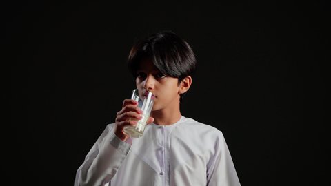 اتباع نظام غذائي صحي، فوائد مشتقات اللبن المتعددة للجسم والعظام, بورتريه مقرب لولد عربي خليجي سعودي يرتدي الثوب الابيض يقوم بشرب كأس من الحليب، المحافظة على سلامة الجهاز المناعي، مفهوم العناية والاهتمام بالصحة, خلفية سوداء