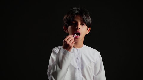 الاهتمام والعناية بنظافة وصحة الفم، تجنب التسوس وأمراض اللثة، تبييض وتجميل ومعالجة الأسنان, التأكد من النظافة بعد تناول الطعام, بورتريه مقرب لولد عربي خليجي اماراتي يرتدي الكندورة يقوم بتنظيف اسنانه باستخدام الخلال البلاستيكي, خلفية سوداء