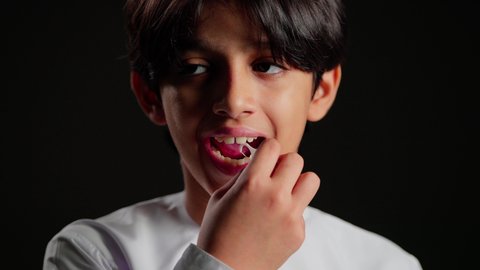 تجنب التسوس وأمراض اللثة، الاهتمام والعناية بنظافة وصحة الفم، تبييض وتجميل ومعالجة الأسنان, التأكد من النظافة بعد تناول الطعام, بورتريه مقرب لولد عربي خليجي اماراتي يرتدي الكندورة يقوم بتنظيف اسنانه باستخدام الخلال البلاستيكي, خلفية سوداء