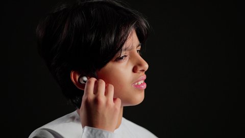 سماعة بلوتوث حديثه، بورتريه مقرب لولد عربي خليجي اماراتي يرتدي الكندورة يمسك بيديه سماعته الاسلكيه ، مفهوم إستخدام إكسسوارات الجهاز المحمول، أجهزه وتقنيه المحمول، خلفية سوداء