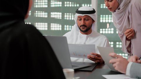 Reviewing work reports, using technology and modern techniques in work, studying new projects, the concept of economic growth and financial investment, following up on the chart, auditing and analyzing project data, Arab Gulf and Emirati work friends analyzing data on a laptop