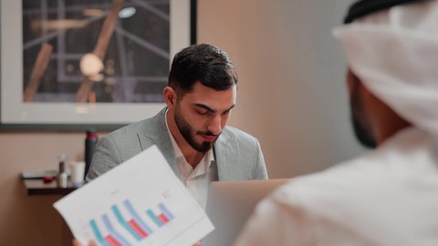 متابعة مخطط الرسم البياني، تدقيق وتحليل بيانات المشروع،  استخدام التكنولوجيا والتقنيات الحديثة فى العمل ، دراسة مشاريع جديدة، زميلان عمل عربيان خليجيان اماراتيان يقومان بتحليل البيانات على الحاسوب المحمول، مفهوم النمو الاقتصادي والاستثمار المالي
