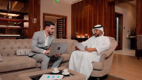 Working remotely, studying new projects, the concept of economic growth and financial investment, following a chart, auditing and analyzing project data, two Arab Gulf Emirati colleagues analyzing data on a laptop