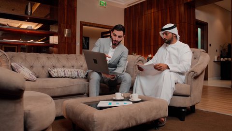 Following a flowchart, reviewing and analyzing project data, using modern technology and techniques in work, studying new projects, two Arab Gulf Emirati colleagues analyzing data on a laptop, the concept of economic growth and financial investment