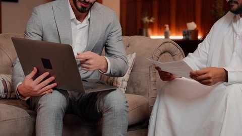 Using modern technology and techniques in work, auditing and analyzing project data, studying new projects, a group of two Arab Gulf Emirati business friends analyzing data on a laptop, following a graph chart, the concept of economic growth and financial investment