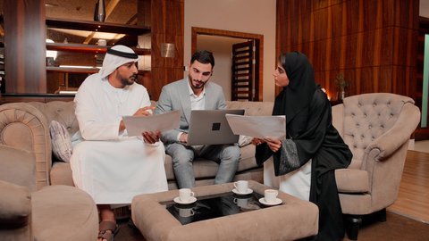 Reviewing work reports, using technology and modern techniques in work, studying new projects, the concept of economic growth and financial investment, following up on the chart, auditing and analyzing project data, Arab Gulf and Emirati work friends analyzing data on a laptop