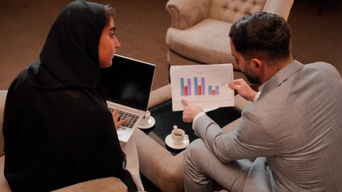 Project data audit and analysis, new project study, two Emirati Gulf Arab colleagues analyzing data on laptop, following a chart, concept of economic growth and financial investment