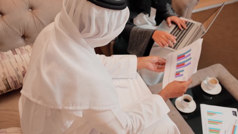 استخدام التقنيات الحديثة فى العمل ، زميلان عمل عربيان خليجيان اماراتيان يقومان بتحليل البيانات على الحاسوب المحمول، متابعة مخطط الرسم البياني، تدقيق وتحليل بيانات المشروع، دراسة مشاريع جديدة، مفهوم النمو الاقتصادي والاستثمار المالي