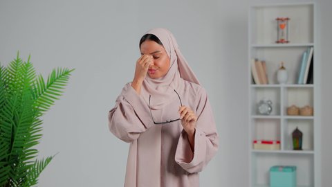 اتباع تعليمات الطبيب، معالجة حالات التهاب العصب البصري، العناية بالعين والحاجة لتعقيمها بشكل مستمر،  ضرورة الذهاب للطبيب والحصول على العلاج، إيماءات التعب والحاجة للراحة،  بورتريه لشابة عربية خليجية إماراتية محجبة ترتدي العباءة تشعر تضع نظارات طبية، خلفية رمادي