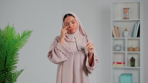 إيماءات التعب والحاجة للراحة، اتباع تعليمات الطبيب، معالجة حالات التهاب العصب البصري، العناية بالعين والحاجة لتعقيمها بشكل مستمر،  ضرورة الذهاب للطبيب والحصول على العلاج، بورتريه لشابة عربية خليجية إماراتية محجبة ترتدي العباءة تشعر تضع نظارات طبية، خلفية رمادي