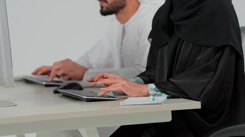 النقر على لوحة المفاتيح، مهن ووظائف مكتبية اماراتية، دمج العمل مع التكنولوجيا الحديثة والمتطورة، الرد والاجابة على الاستفسارات والاستعلامات، استخدام تقنية الهيدفون,  تصوير مقرب ليد امراة عربيه خليجيه اماراتية ترتدي العباءة و الحجاب تجلس امام الحاسب الالى تعمل في مجال خدمة العملاء والدعم الفني برفقة زميلها