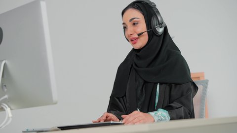 مكالمات فيديو خلال اجتماع العمل, تمكين عمل المرأة في المجتمع السعودي, إمرأة عربية خليجية سعودية محجبة ترتدي عباءة سوداء تضع سماعات الهيدفون تعمل في مجال خدمة العملاء, الرد على الاستعلامات والاستفسارات، استخدام التقنيات الحديثة والمتطورة