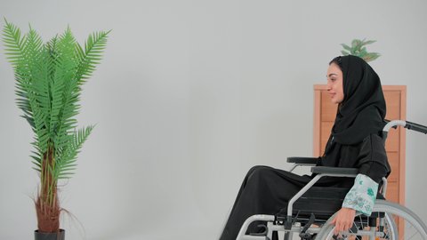 تصوير من الجانب لسيده عربيه خليجيه سعوديه محجبه ترتدي العباءه السوداء تجلس على كرسي متحرك من ذوي أصحاب الهمم تقوم بتحريكه بنفسها،  تحسين حياة ذوي الاعاقه الحركيه للمساعده على التنقل، الحفاظ على الصحة البدنية من خلال تحريك اليدين أثناء الحركة