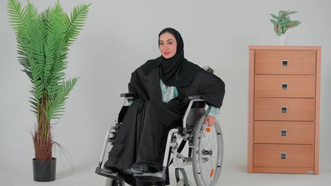 الحفاظ على الصحة البدنية من خلال تحريك اليدين أثناء الحركة, تحسين حياة ذوي الاعاقه الحركيه للمساعده على التنقل, سيده عربيه خليجيه سعوديه محجبه  ترتدي العباءه السوداء تجلس على كرسي متحرك من ذوي أصحاب الهمم تقوم بتحريكه بنفسها