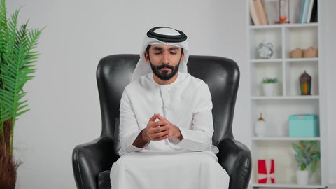 تعابير شرود الذهن والتمعن، ايجاد حل لمشكلة ما، التأمل والتخطيط للمستقبل، رجل عربي خليجي اماراتي يرتدي الكندورة و الغتره يجلس على كرسي يضع يده على ذقنه بايماءات التفكير والتركيز