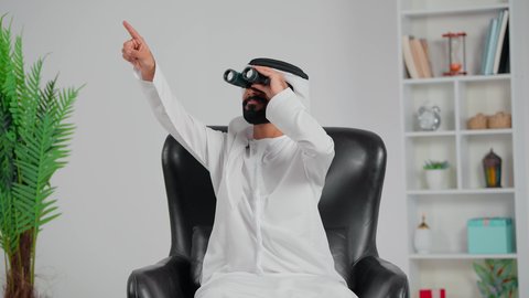 Seeing distant things through a telescope, future planning for goals and ambitions, love for exploration and adventure, an Arab Gulf Emirati man wearing a kandura and ghutrah sitting on a chair looking through binoculars, pointing at something.