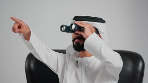 التخطيط المستقبلي للأهداف و الطموحات، رؤية الاشياء البعيدة عبر التلسكوب، حب الاستكشاف والمغامرة، تصوير مقرب لرجل عربي خليجي اماراتي يرتدي الكندورة و الغتره يجلس على كرسي  ينظرمن خلال منظار ثنائي العينين، الاشارة الى شيء ما