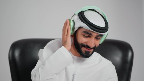 الإستماع للأغاني بإستخدام الهيدفون، الاندماج والتفاعل مع الانغام الموسيقية، تعابير وايماءات السرور لسماع الأغنية، تصوير مقرب لرجل عربي خليجي اماراتي يرتدي الكندورة و الغتره يضع سماعة رأس, مواهب غنائية فنية