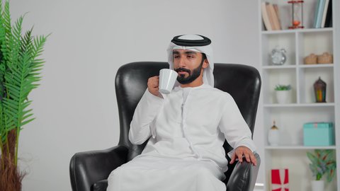الشعور بالانتعاش والفرح, احتساء المشروب الساخن، رجل عربي خليجي اماراتي يرتدي الكندورة و الغتره يجلس على كرسي يحمل فنجان من الشاي، الاستمتاع بلحظات الهدوء والراحة